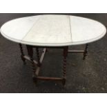 An oval oak dining table with painted moulded top having two drop-leaves, raised on barleytwist