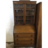 A 1930s oak bureau bookcase, the astragel glazed top with press moulded decoration having glazed