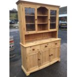 A pine dresser with moulded cornice above leaded glass doors flanking open shelves framed by