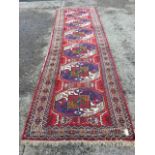 An oriental runner woven with six aztec patterned octagonal geometric medallions on red ground,