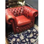 A red leather chesterfield style armchair with button upholstery and loose cushion, having