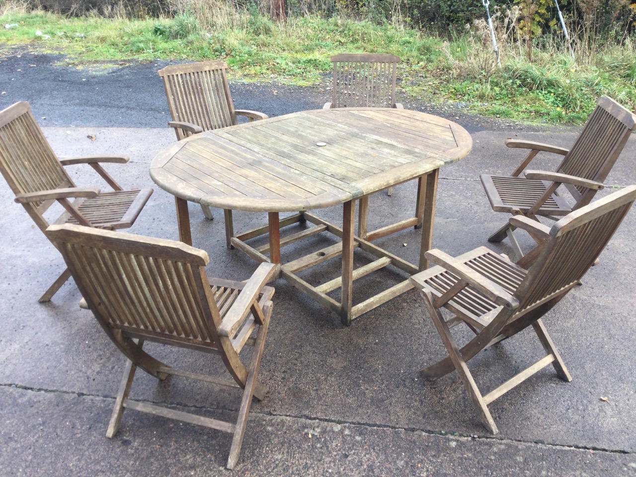 A teak garden suite, the oval slatted table with drop leaves on rectangular frame, the six folding