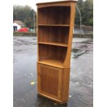 An Ercol oak corner cabinet with shaped apron above illuminated open shelves, with panelled door