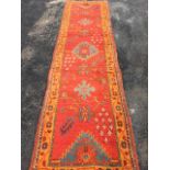 A Turkey runner, the red field woven with serrated, star & floral motifs framed by orange border