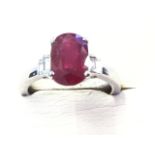 An 18ct white gold ruby & diamond ring, the oval claw set ruby weighing over three carats, raised