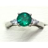 An 18ct white gold emerald & diamond ring, the circular claw set emerald weighing over a carat,
