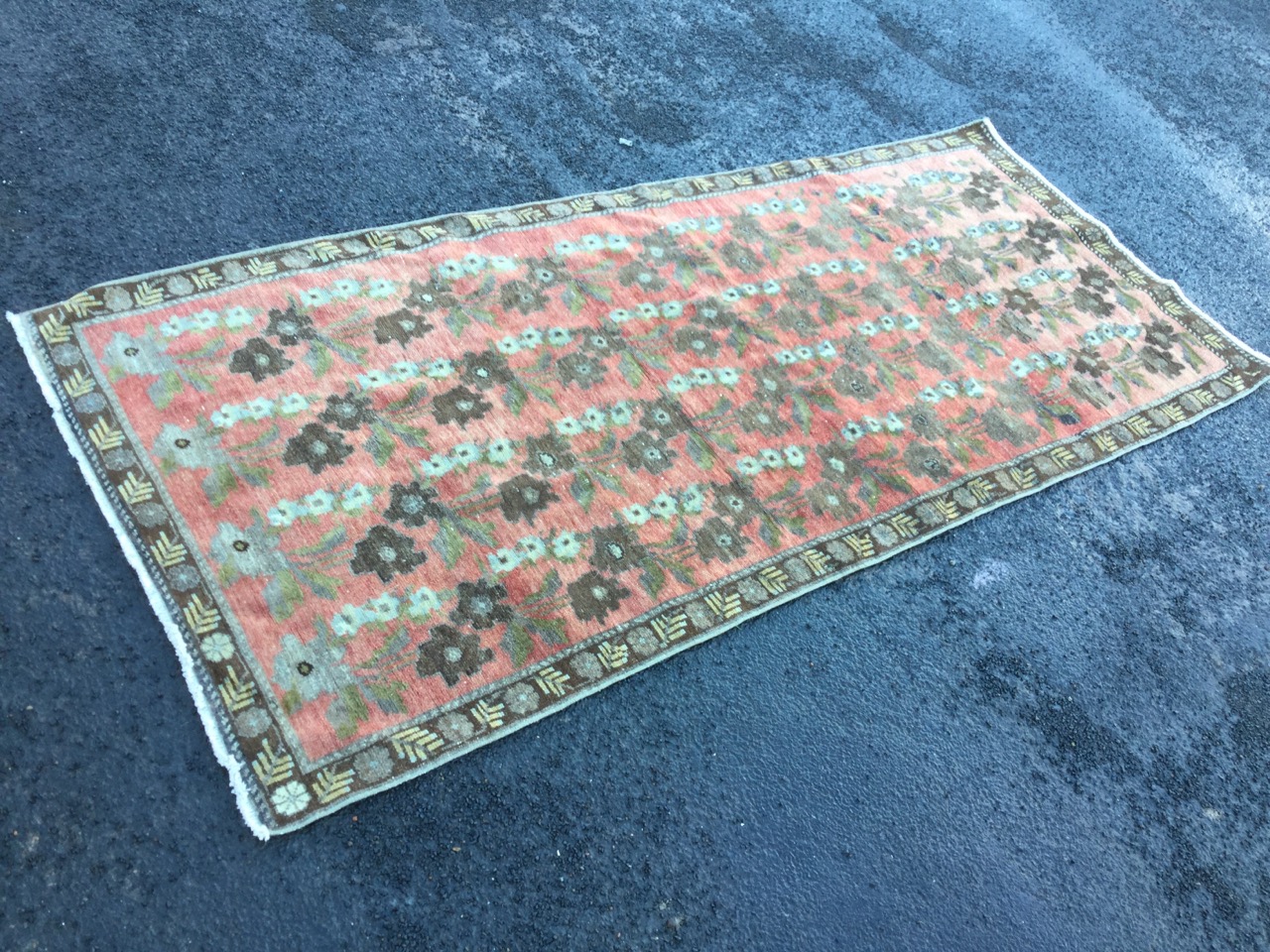 An oriental rug woven with floral designs in pink field framed by brown border with leaf and