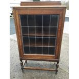 A glazed oak cabinet with rectangular moulded top above leaded glass door, raised on turned legs