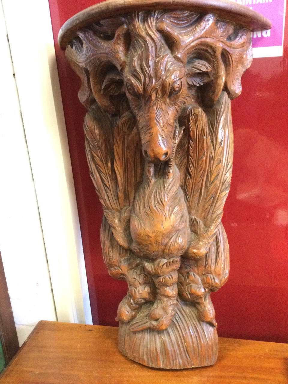 A carved hardwood wallshelf, the ‘D’ shaped moulded top on a corbel carved with feathered game &