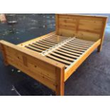 A pine double bed, the panelled headboard and tailboard with shelf tops, having solid square