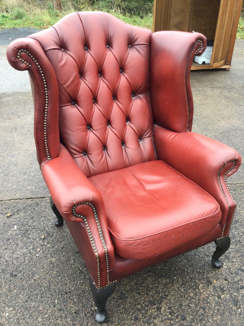 A Queen Anne style button upholstered wing armchair with brass studding, raised on cabriole legs.