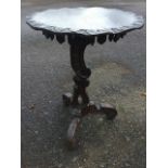 A carved oak rustic table, the circular top with leaf carved waved border above a dentil applied