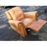 A tan leather reclining arcmchair, the cushion back with brass studding above a sprung cushion