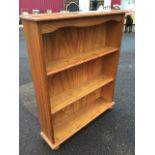 A pine open bookcase with rectangular moulded top above a waved apron and open shelves, raised on