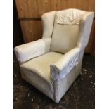 An upholstered wingback armchair in cream damask, with padded back above a sprung seat raised on bun