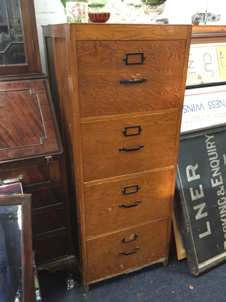 A large wood filing cabinet, the four drawers mounted with metal handles and label holders. (20in