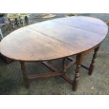 An oval oak dining table, the top with two drop leaves supported on baluster turned columns joined