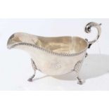 George V silver sauce boat of helmet form with gadrooned borders and scroll handle, raised on three