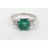 Emerald and diamond three stone ring with a square step-cut emerald measuring approximately 7.50mm x
