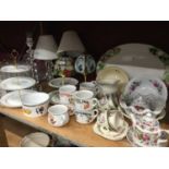 Two shelves of china and glassware to include collectors plates, and Tiffany style table lamp