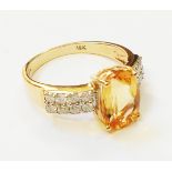 A hallmarked 750 yellow gold ring, set with central oval citrine flanked by diamond encrusted