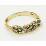 A yellow metal ring set with three small emeralds interspersed with pairs of tiny diamonds
