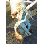 A painted cast iron garden cherub sat weeping on a finial