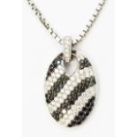A hallmarked 750 white gold oval pendant encrusted with meandering rows of black and white diamonds,