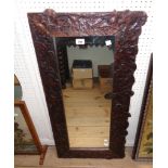 A varnished and stained carved wood framed narrow oblong wall mirror, with trailing foliate