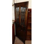 A 28" James Lupton & Sons polished oak corner cabinet with leaded glazed panel doors to top and