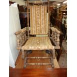 An antique American stained wood framed rocking chair with slung upholstery and turned spindle