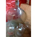 Two old glass demijohns with wine merchant labels, one other, and a large vintage carboy