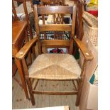 An old stained beech framed ladder back elbow chair with woven rush seat and simple turned supports