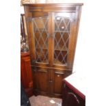 A 28" James Lupton & Sons polished oak corner cabinet with leaded glazed panel doors to top and