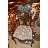 A late Victorian ebonised framed elbow chair with ornate top rail, pierced splat back and