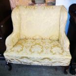 An antique wing back two seater settee with floral pattern old gold upholstery, set on mahogany