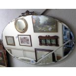 A vintage frameless bevelled oval wall mirror with decorative cast metal pediment