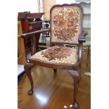 An early 20th Century stained walnut framed panel back elbow chair upholstered in floral tapestry,