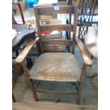 An old stained beech framed ladder back elbow chair with woven rush seat and simple turned supports