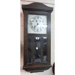 An early 20th Century stained oak cased wall clock with visible pendulum and gong striking