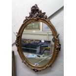 A decorative gilt plaster framed oval wall mirror with Rococo style pediment and floral decoration -