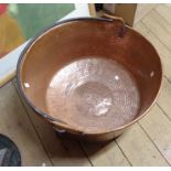 A large copper pan with hammered decoration and swing iron handle