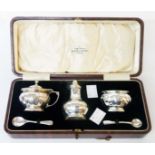 A cased silver three piece condiment set of faceted baluster design with blue glass liners -