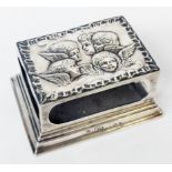 An Edwardian silver table matchbox sleeve with cherub group decoration to top, set on loaded stepped