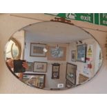 A vintage frameless bevelled oval wall mirror with decorative cast and brassed pediment