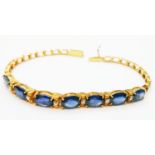 A marked 750 yellow metal bracelet, set with seven oval sapphires interspersed with tiny diamonds