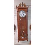 A modern stained wood cased regulator style wall clock with large visible pendulum, two pulleys