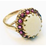 A hallmarked 375 gold ring, set with large central oval milky opal within a ruby encrusted border