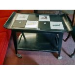 A retro ebonised wood two tier tea trolley with vintage motor car tiled top, set on moulded