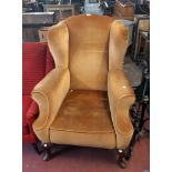 A late 19th/early 20th Century wing back armchair with old gold velour upholstery, set on heavy